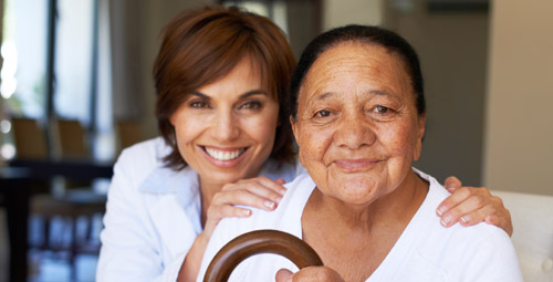 Elderly lady seated with a younger lady crouched next to her with her hands on her shoulders